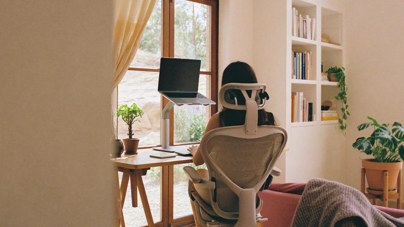 Mujer teletrabajando en casa con el portátil elevado y teclado externo